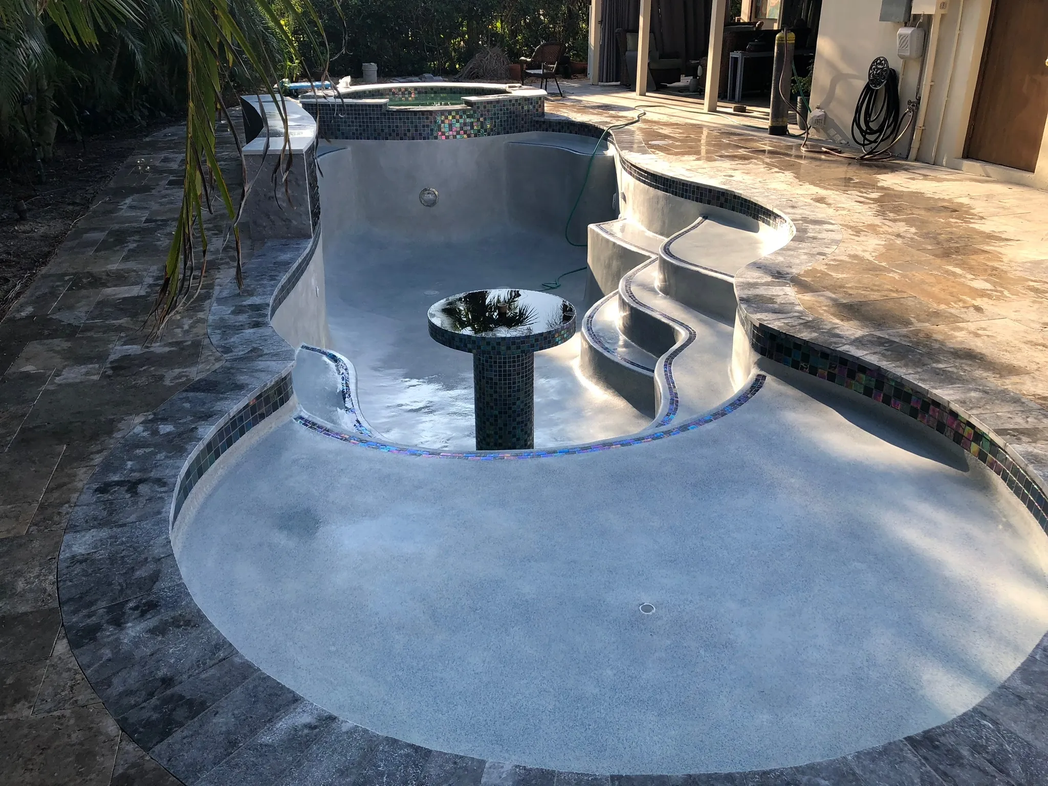 Freeform pool with built-in steps, a central fountain bowl, and dark stone coping.