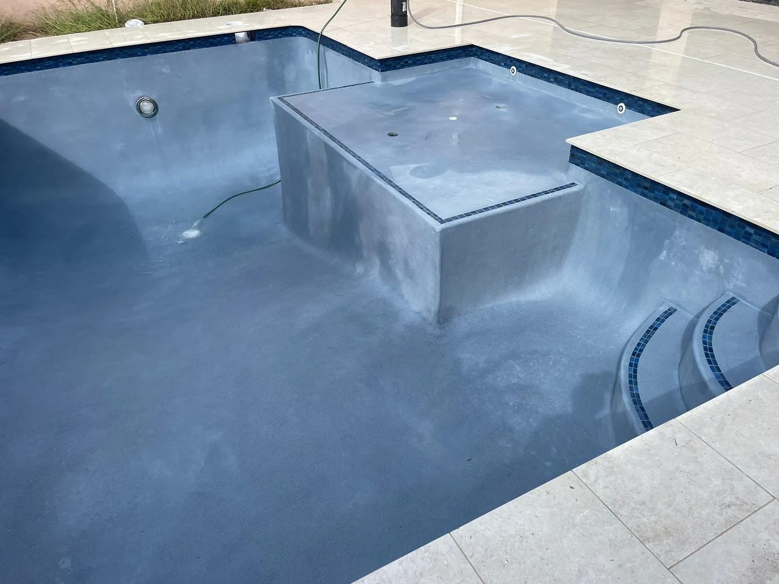 A raised bench with steps inside a pool with a smooth gray-blue finish.