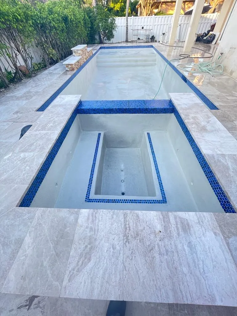 Long pool and an inset spa with blue waterline tile and light stone coping.