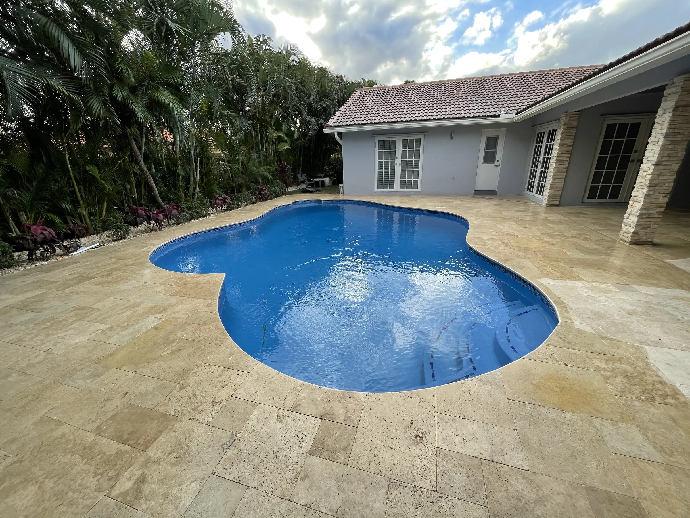 A finished freeform pool and wide paver deck seen from the corner of the yard.