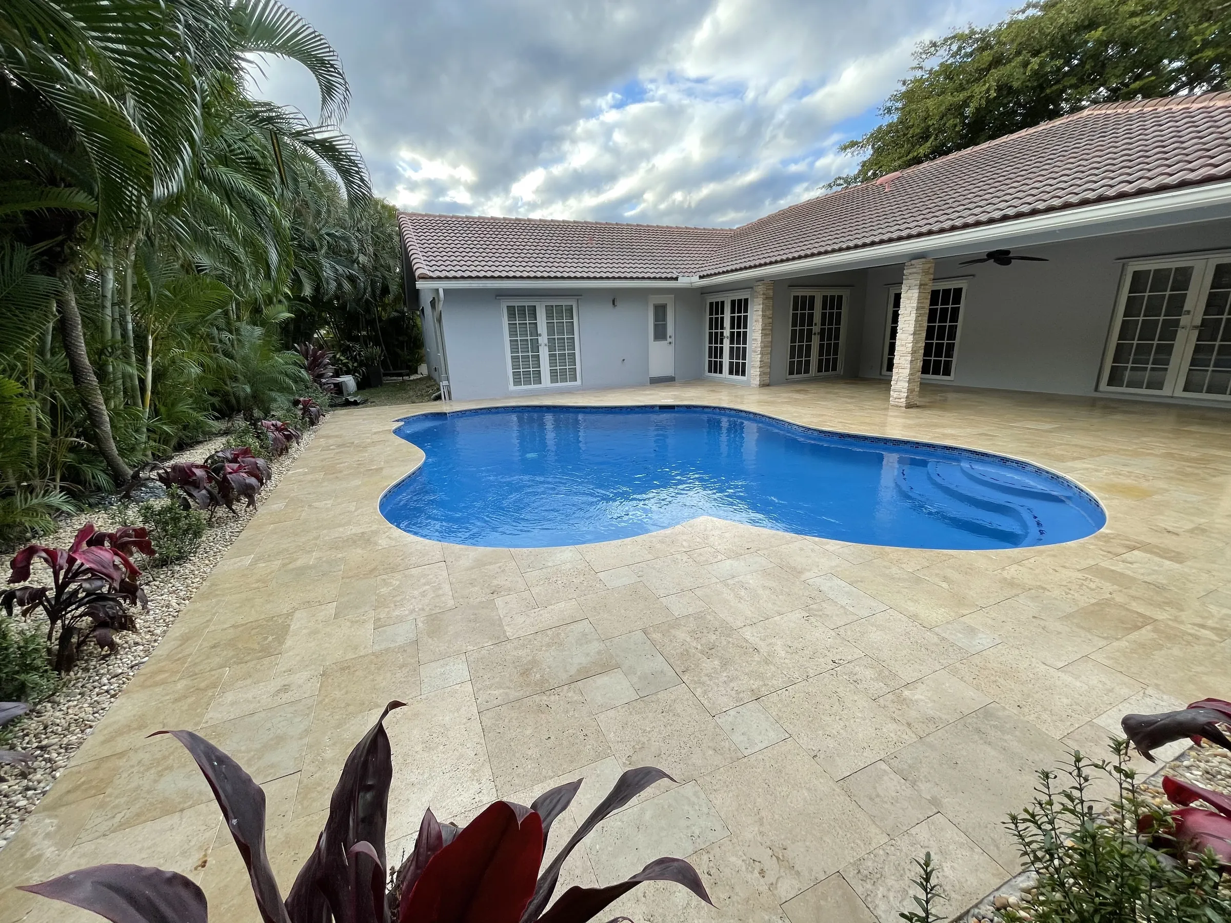 Finished pool and stone-look deck with tropical planting in the foreground.