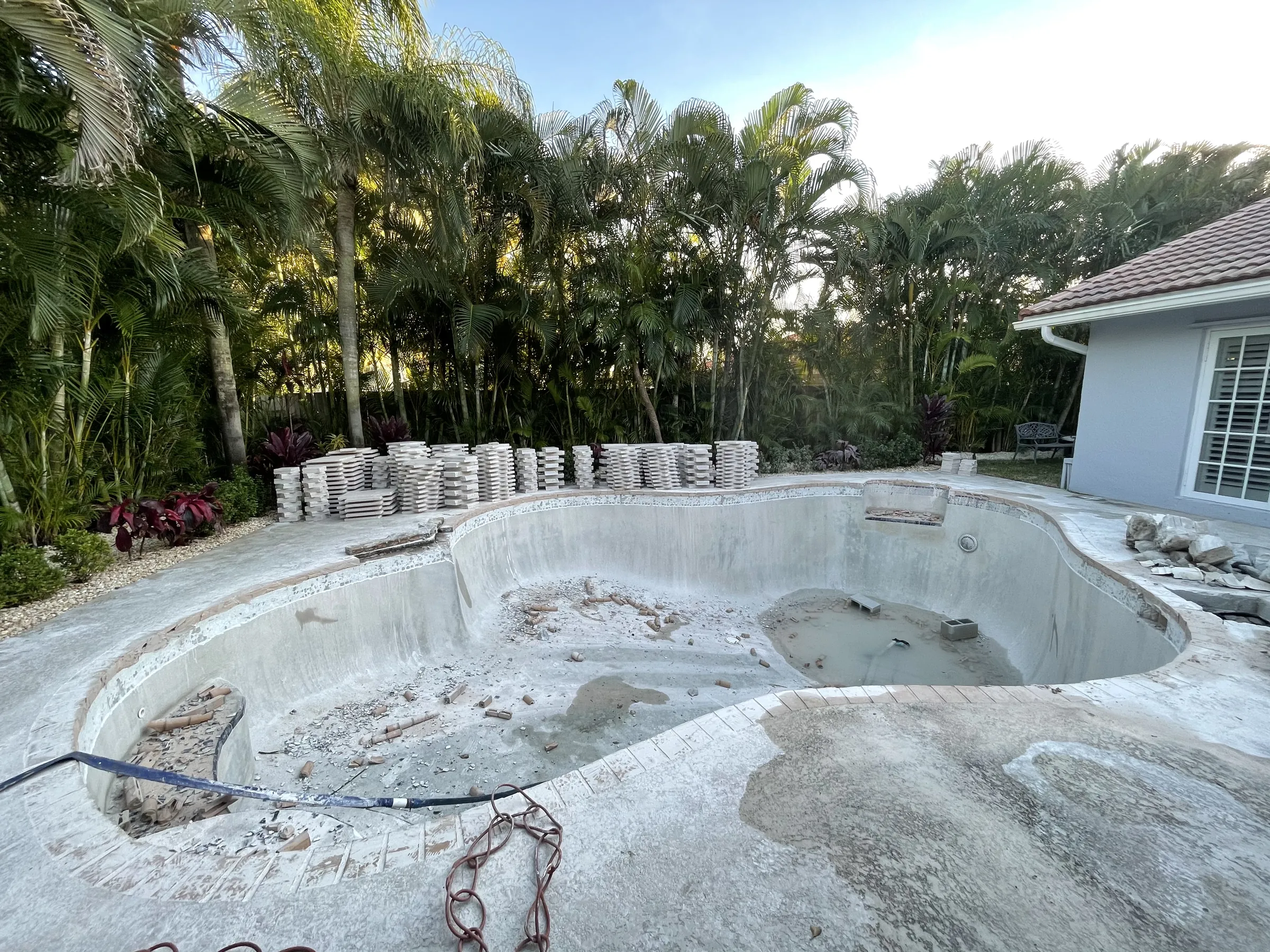 Before: the old pool opened up to bare plaster, with new deck pavers stacked along the edge.