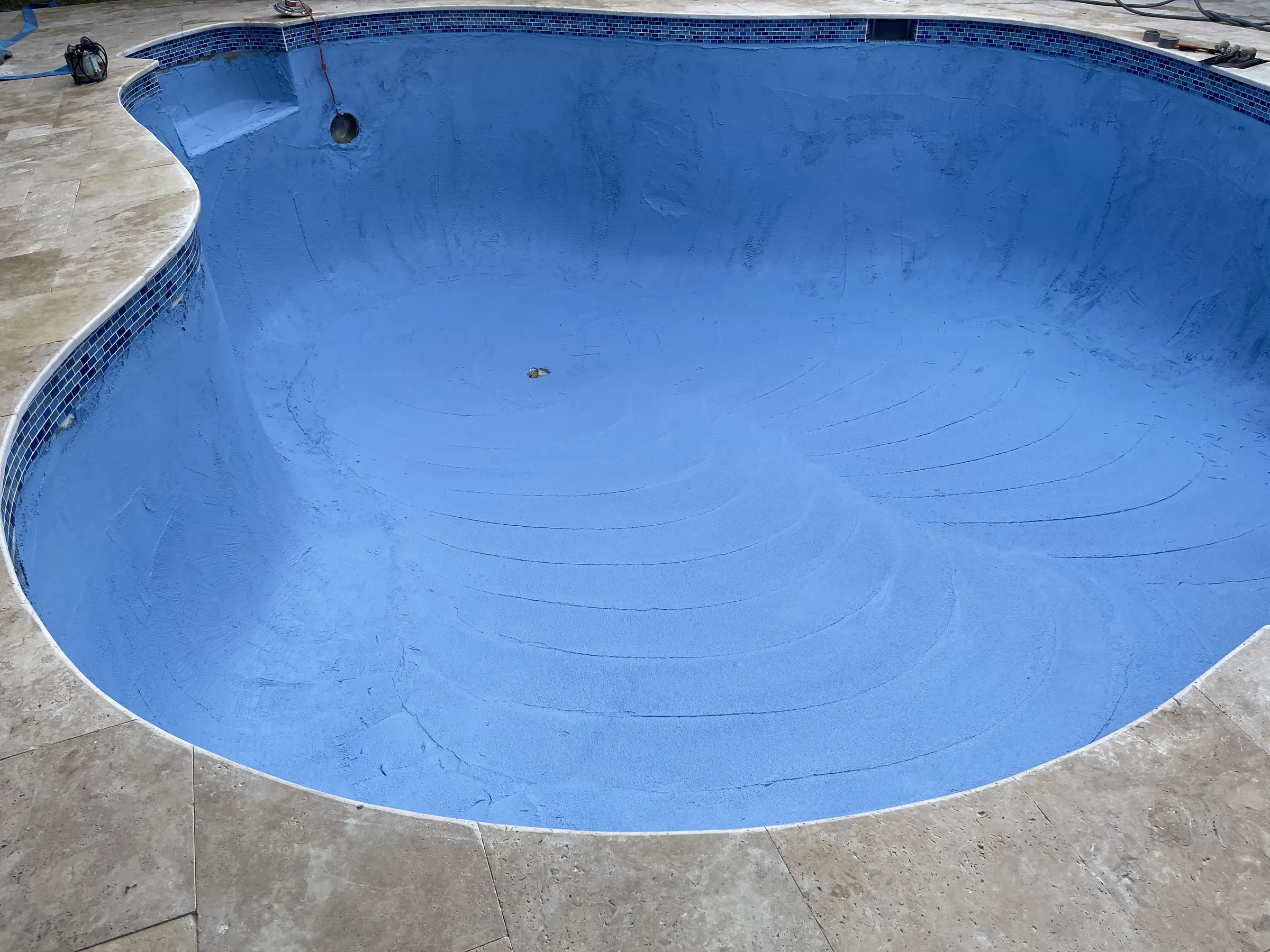 An empty pool with a fresh, smooth blue interior finish and mosaic waterline tile.