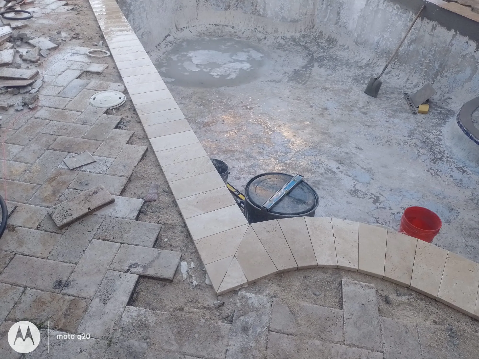 Coping and deck pavers being laid around an open pool shell.