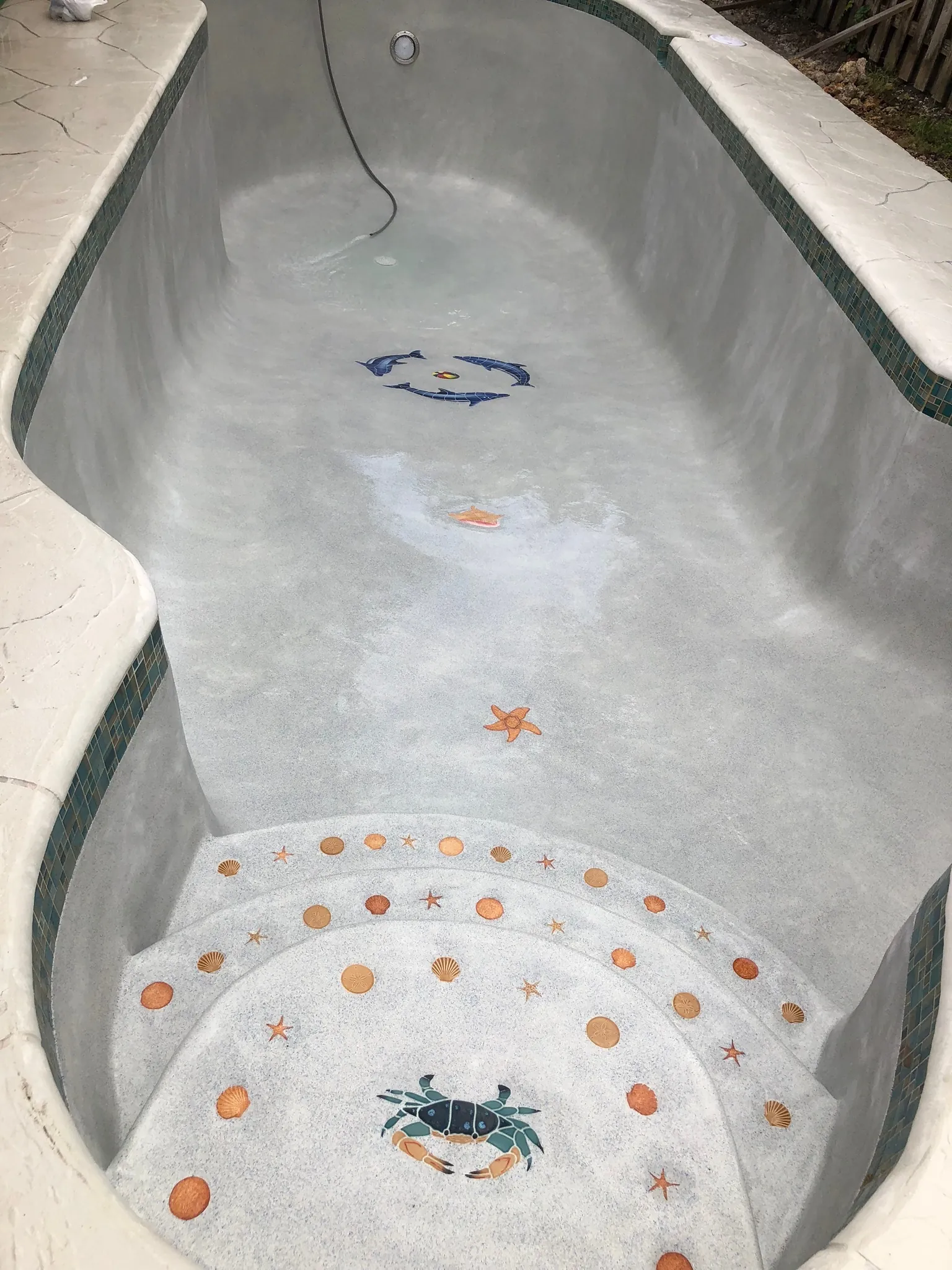 A mosaic of a crab and shells set into a pool floor.